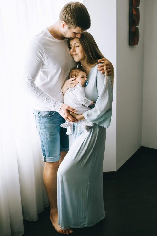 happy-family-carrying-little-baby-boy-in-front-of-curtains-at-home.jpg
